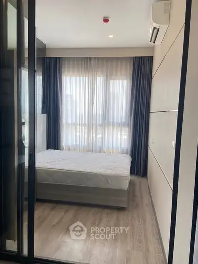 Modern bedroom with large windows and wooden flooring, featuring sleek design and natural light.