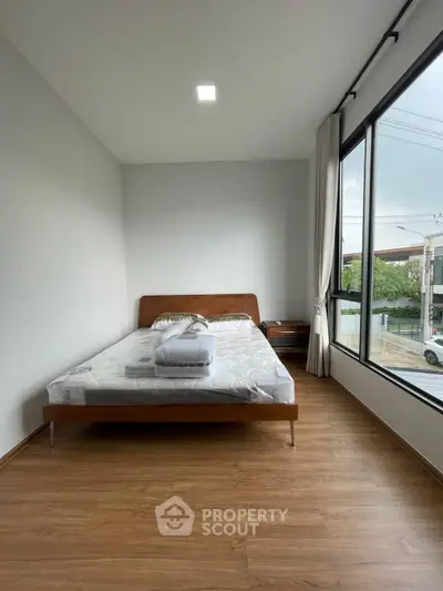 Modern minimalist bedroom with large window and wooden flooring