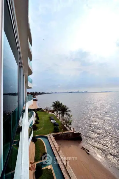 Stunning waterfront view from modern apartment building with lush garden and city skyline in the distance.