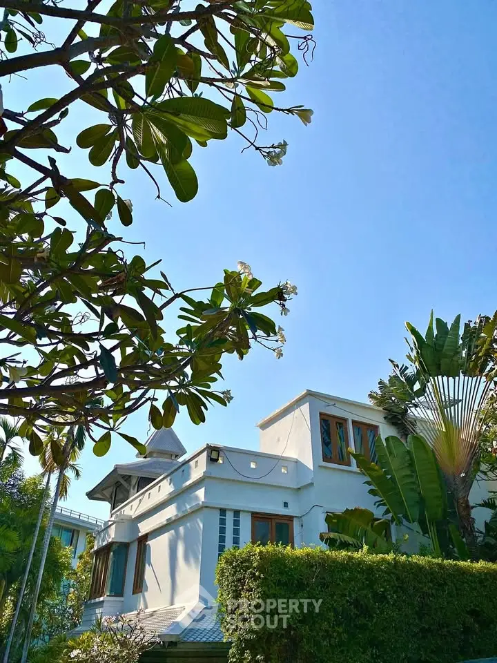 Charming villa with lush garden and modern architecture under clear blue sky.
