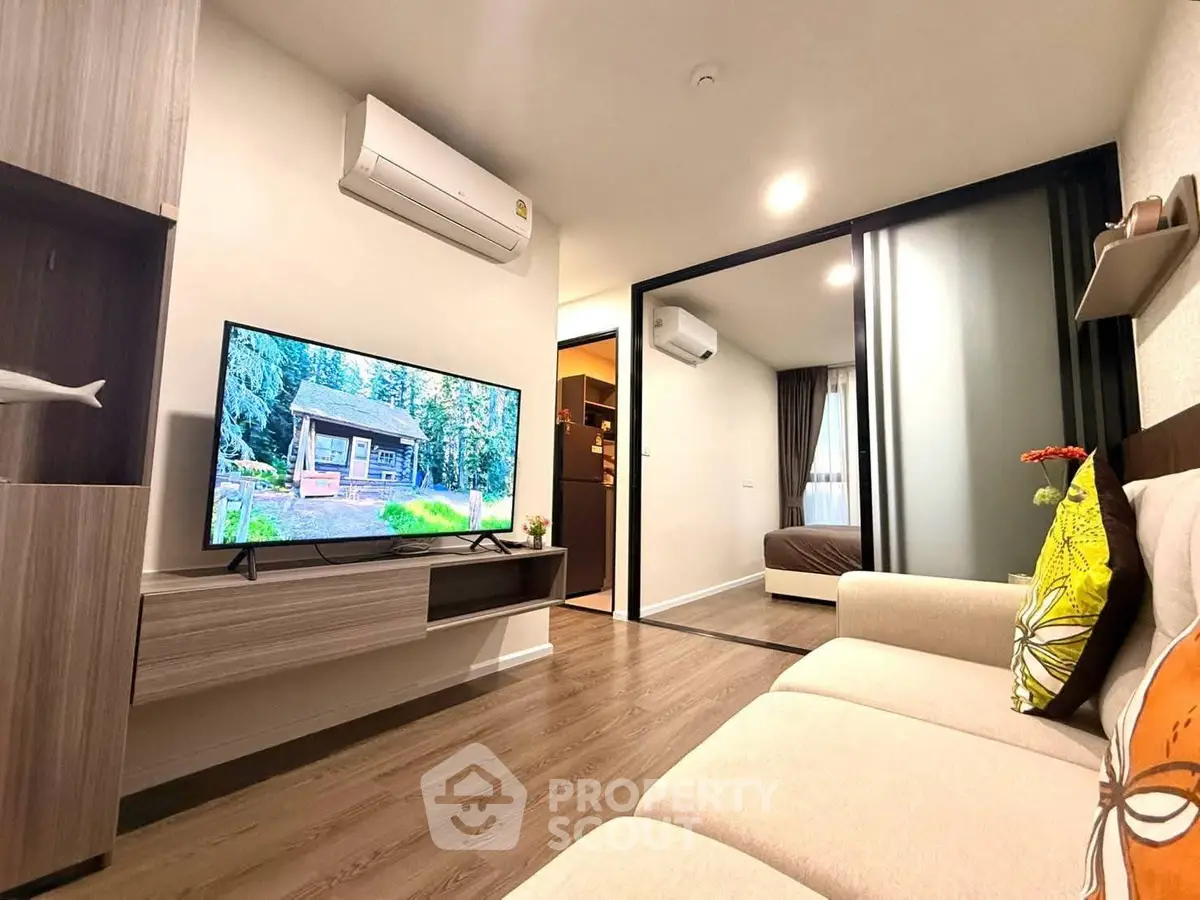 Modern living room with cozy sofa and flat-screen TV, open view to bedroom, stylish interior design.