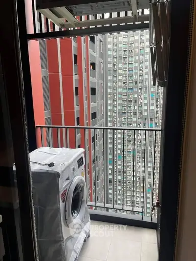 Compact balcony with washing machine and city view in modern high-rise apartment.