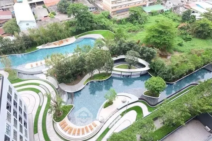 Stunning aerial view of modern apartment complex with lush landscaped gardens and unique pool design.