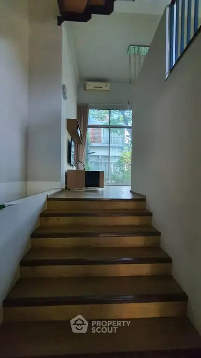 Modern staircase with wooden steps leading to a bright living area with large windows.