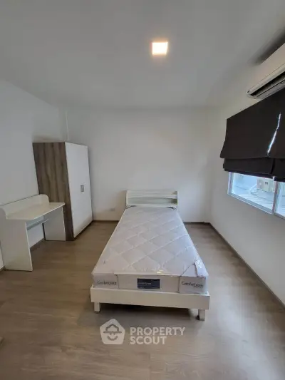 Modern minimalist bedroom with single bed, wardrobe, and desk, featuring sleek wooden flooring and air conditioning.