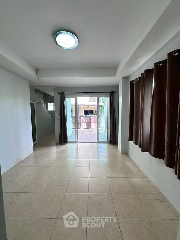 Spacious living room with tiled floor and large windows leading to a balcony.