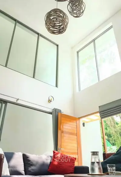 Spacious living room with high ceilings and modern decor, featuring large windows and stylish lighting.