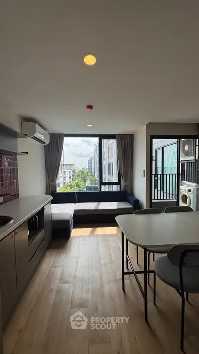 Modern open-layout living room with kitchen, featuring large windows and stylish furniture.