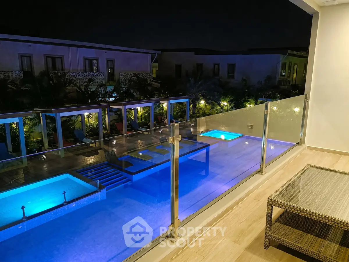 Luxurious night view of illuminated pool from a modern balcony with glass railing.