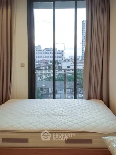 Modern bedroom with large window offering city view, featuring a comfortable bed and elegant curtains.