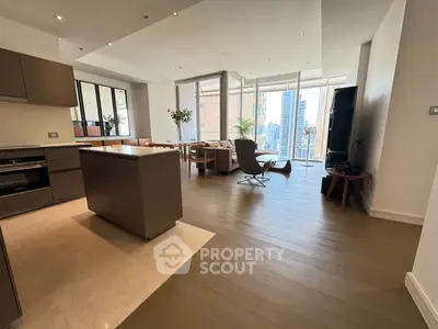 Spacious modern living room with open kitchen and city view, featuring elegant furnishings and natural light.
