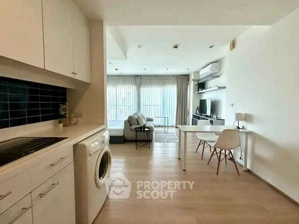 Modern open-plan living room with kitchen and washing machine, bright and airy space.