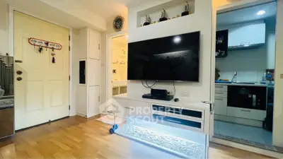 Modern living room with sleek TV setup and open kitchen view, featuring stylish decor and wooden flooring.