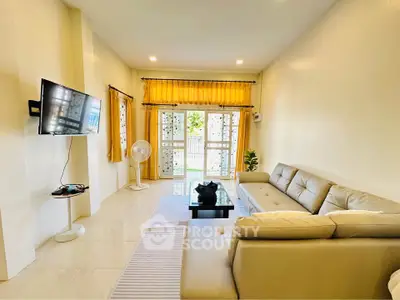Spacious living room with modern decor and natural light, featuring a large sofa and wall-mounted TV.