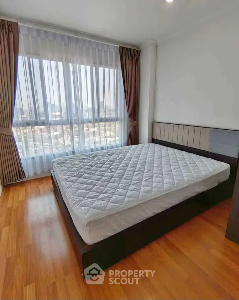 Spacious bedroom with large window offering stunning city views, featuring a comfortable bed and elegant wooden flooring.
