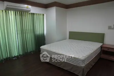 Spacious bedroom with large window and green curtains, featuring a comfortable bed and wooden flooring.