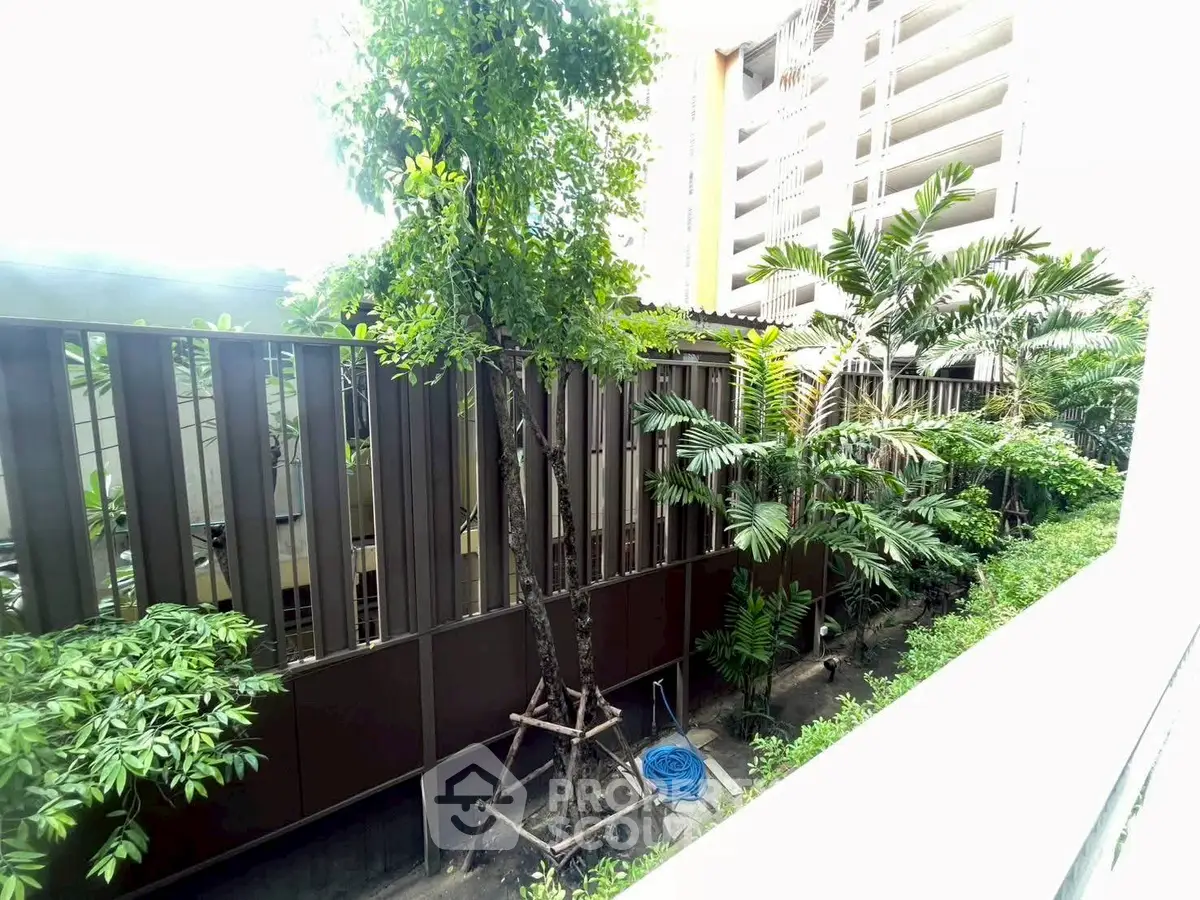 Lush garden view from a modern apartment balcony, showcasing greenery and contemporary architecture.