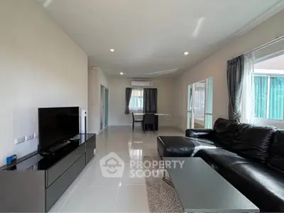 Spacious modern living room with sleek black leather sofa and large TV, perfect for relaxation.