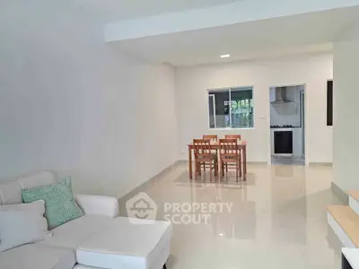 Modern living room with open layout and dining area, featuring sleek furniture and bright lighting.