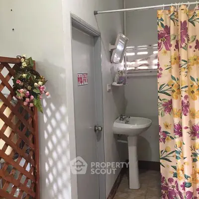 Cozy bathroom with floral shower curtain and pedestal sink, perfect for compact spaces.