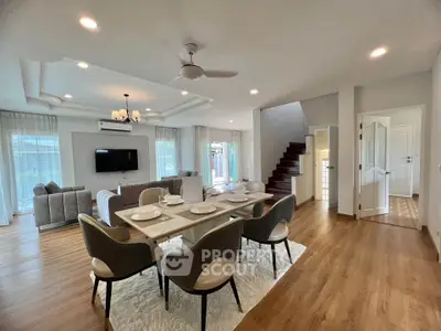 Spacious open-plan living and dining area with modern decor and natural light, featuring elegant furnishings and wooden flooring.