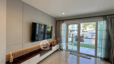 Modern living room with large windows and wall-mounted TV, opening to a garden view.