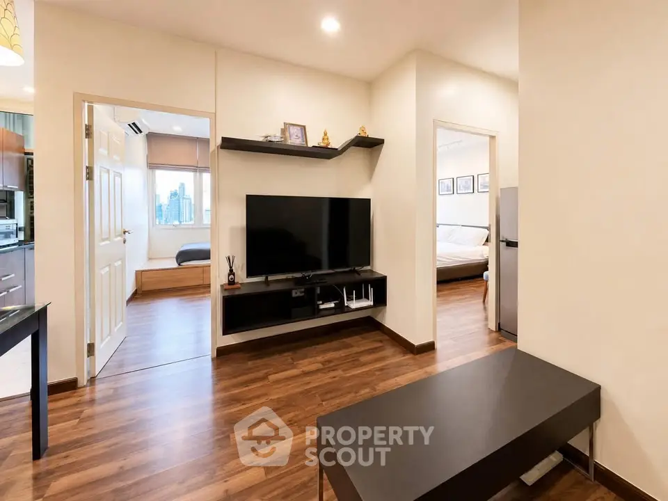 Modern living room with wooden flooring and sleek TV setup, connecting to bedrooms and kitchen.