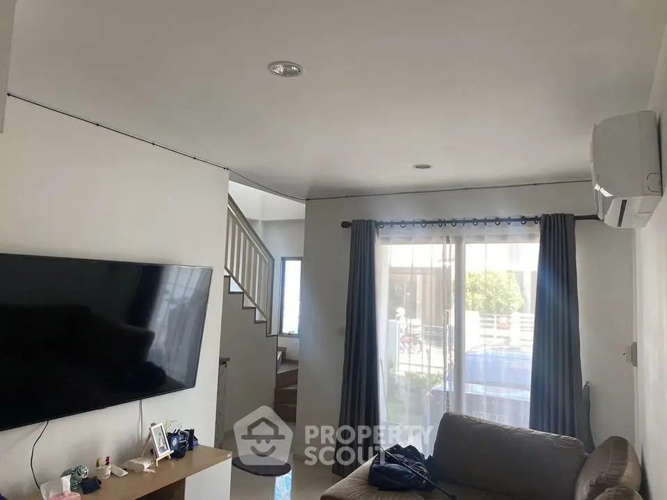 Modern living room with large TV, cozy sofa, and natural light from window.