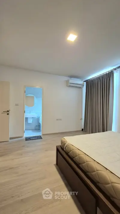 Spacious bedroom with modern design and ensuite bathroom, featuring large windows and air conditioning.
