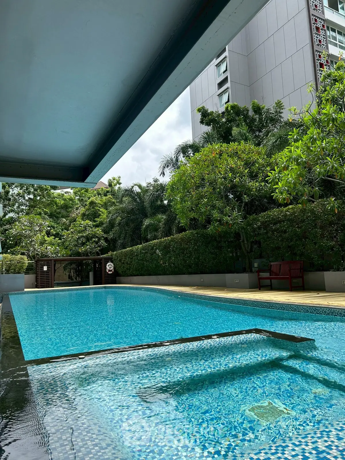 Luxurious outdoor pool area with lush greenery and modern building backdrop.
