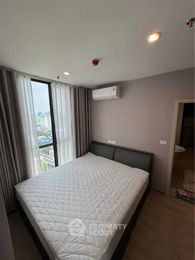 Modern bedroom with large window and city view, featuring a comfortable bed and air conditioning.