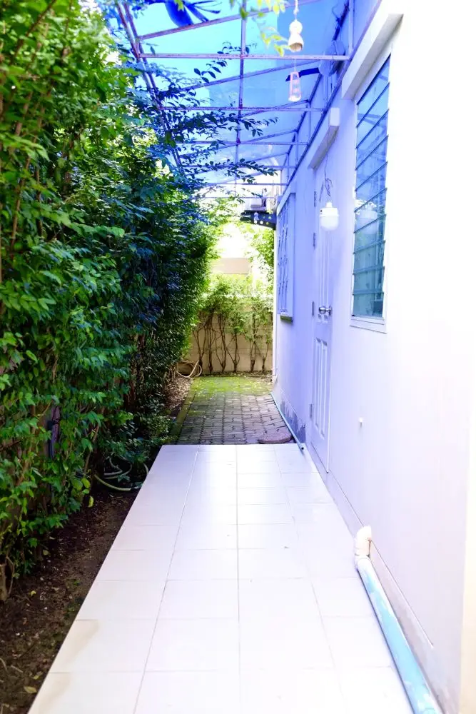 Charming exterior walkway with lush greenery and tiled path leading to a cozy entrance.