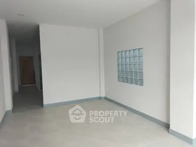 Spacious empty room with modern tile flooring and glass block accent wall.