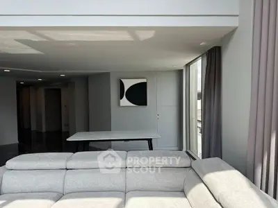 Modern living room with stylish gray sofa and abstract wall art, featuring large windows for natural light.