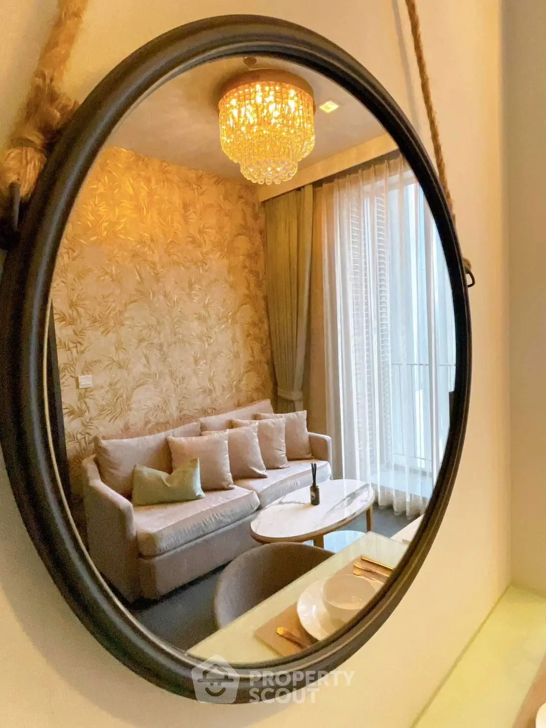 Elegant living room with plush sofa and chandelier reflected in a round mirror, exuding luxury and style.