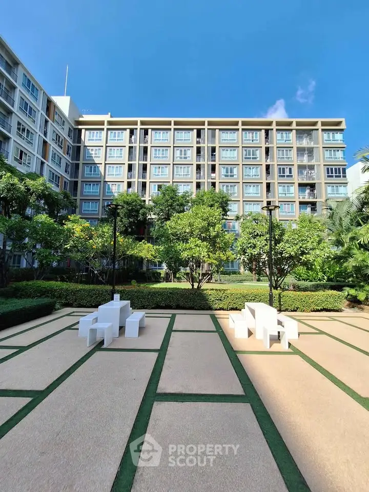 Modern apartment building with lush garden and seating area under clear blue sky.
