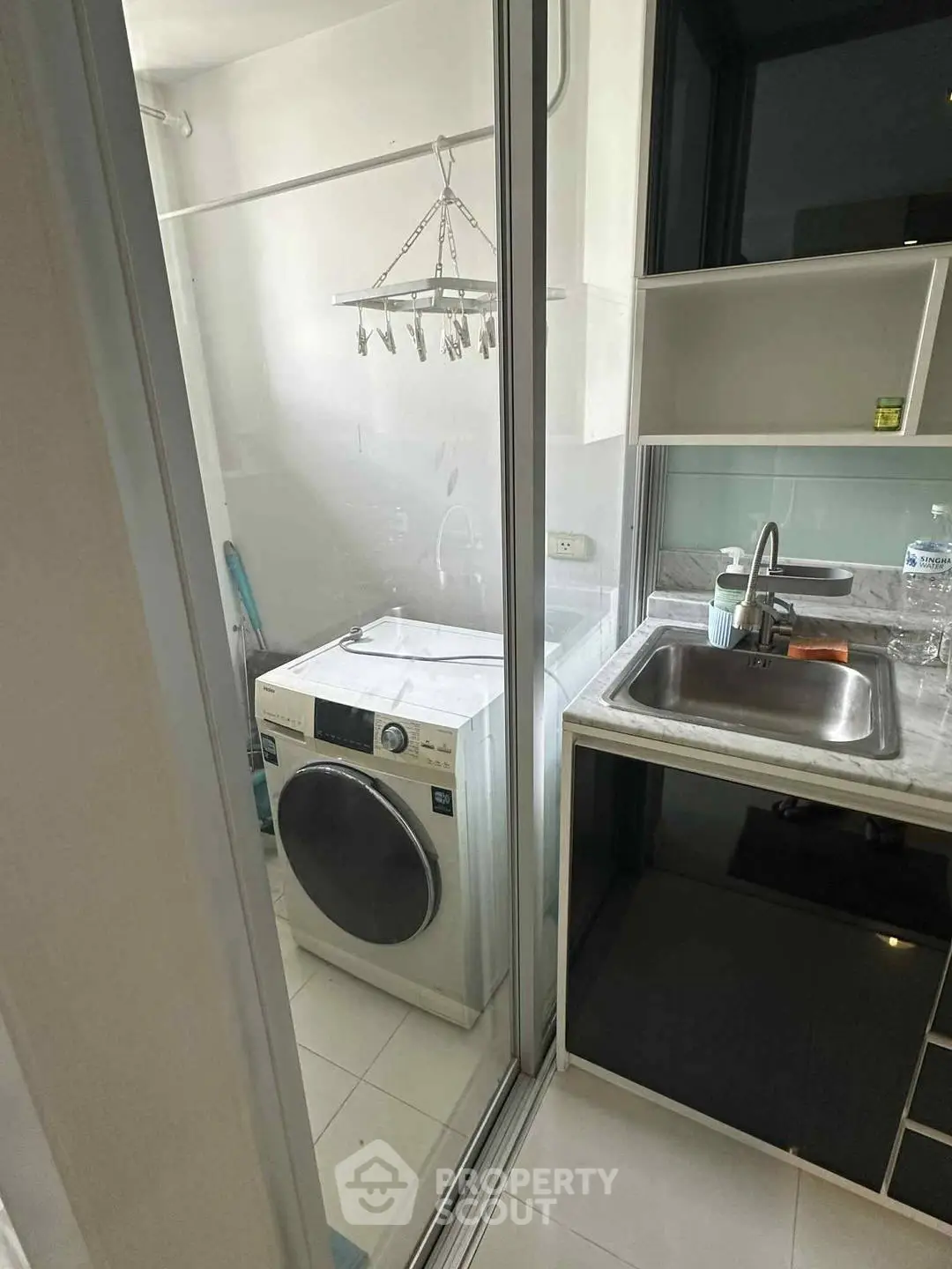 Compact laundry area with modern washing machine and sink in a bright apartment.