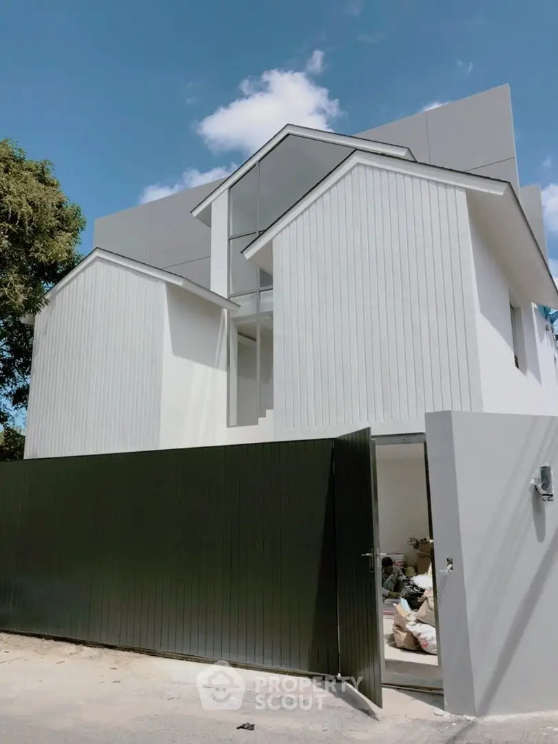 Modern minimalist white house with unique architectural design and open gate under clear blue sky.