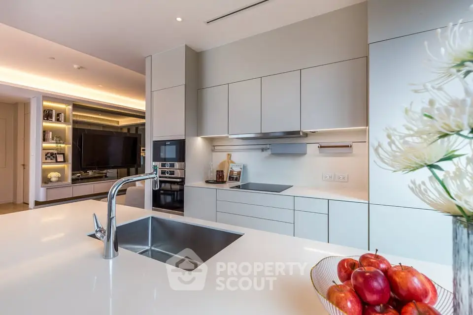 Modern kitchen with sleek cabinetry and built-in appliances, featuring a stylish island with sink and fruit bowl.