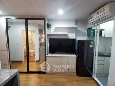 Modern apartment interior with sleek kitchen and cozy living area, featuring a large TV and air conditioning.