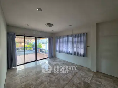 Spacious living room with large windows and balcony access, featuring elegant tiled flooring.