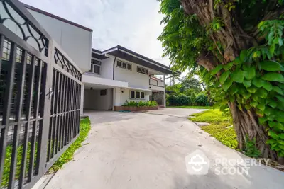 Expansive driveway leading to a spacious two-story home with lush greenery and secure gate, offering a serene and private living experience.