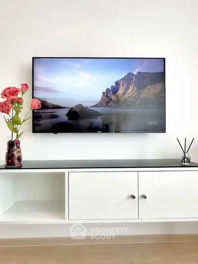 Modern living room with wall-mounted TV and stylish white cabinet, accented by decorative flowers and reed diffuser.