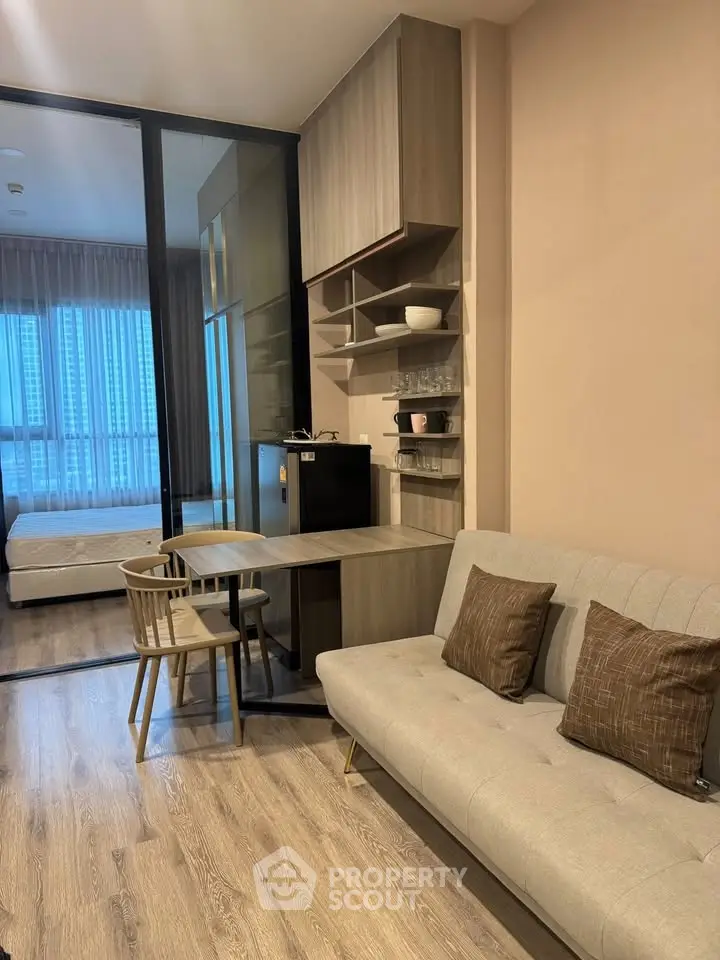 Modern studio apartment with cozy living area and glass partitioned bedroom, featuring stylish furniture and natural light.