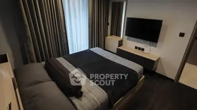 Modern bedroom with sleek furnishings and wall-mounted TV, featuring dark curtains and bedding.