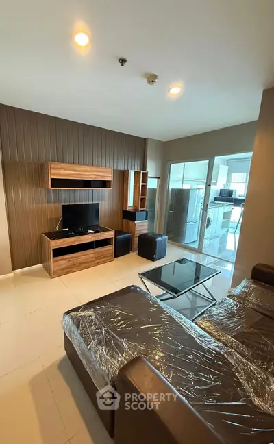 Modern living room with sleek furniture and glass coffee table, featuring a TV and entertainment unit.
