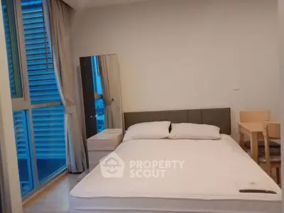 Modern bedroom with large window and minimalist furniture in urban apartment.