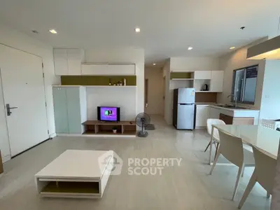 Modern open-plan living room with kitchen, featuring sleek furniture and stainless steel appliances.