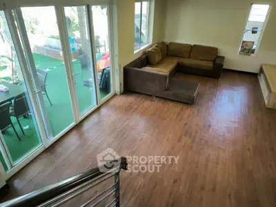 Spacious living room with wooden flooring and large windows opening to a garden view.