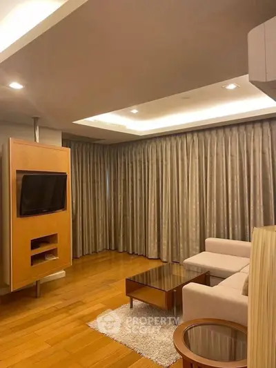 Spacious living room with modern decor and wooden flooring, featuring a cozy seating area and built-in TV unit.